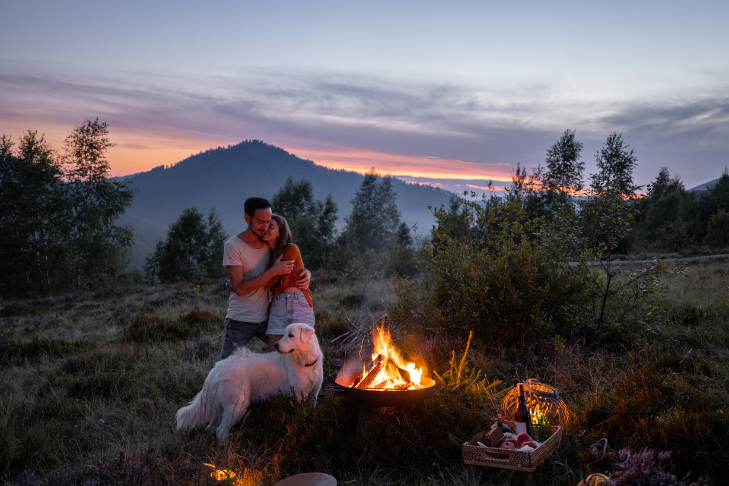 couple on a romantic date, including their dog on the activity, with a bonfire in the mountains