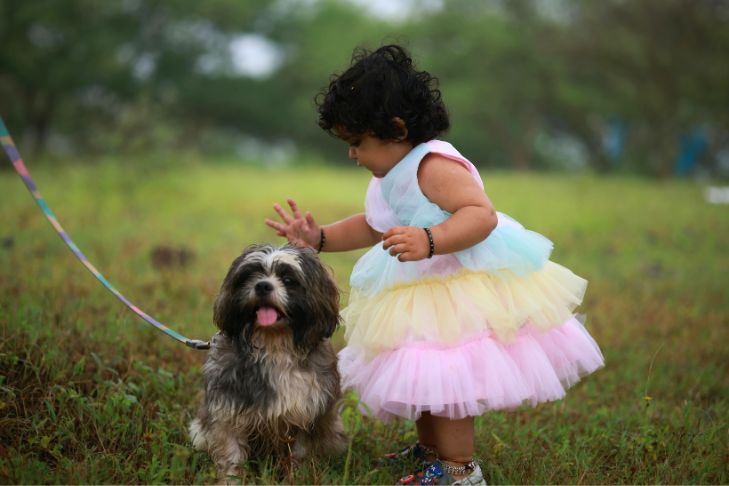Young girl in a pastel dress pets small dog on a leash